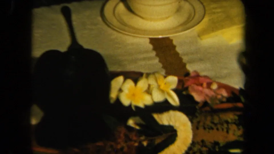 The closing frame emphasizes the decorated table surface with a teacup, candle, flowers, greenery, and a shadowed serving object.