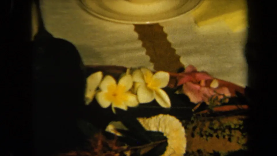 1961 California home-movie frame showing a warm table setting with tropical flowers and patterned linens.