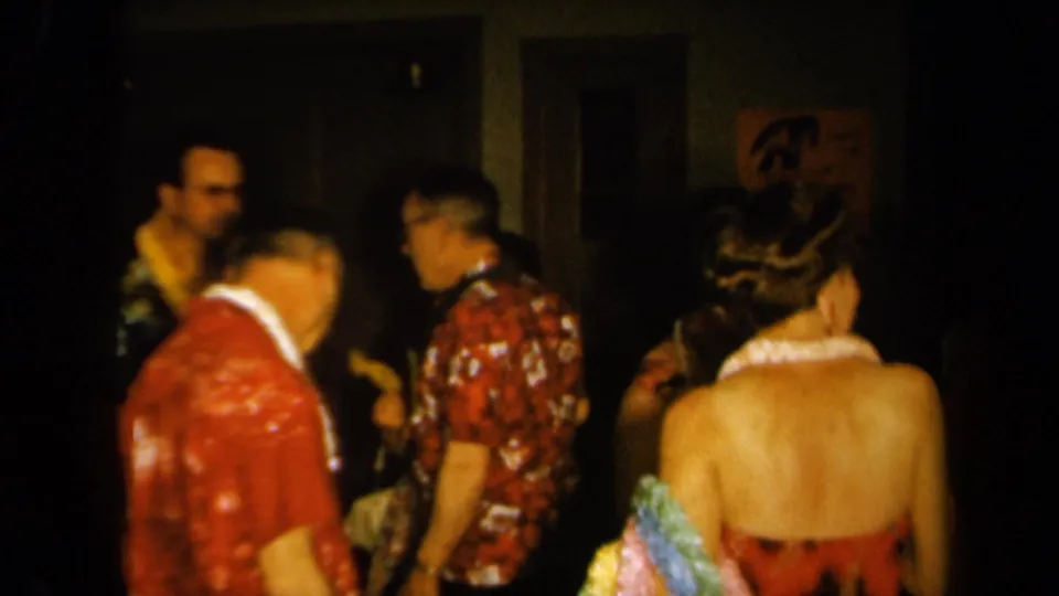 Adults at a 1961 California Hawaiian-themed party mingle in a dim private interior with patterned shirts, leis, and dresses.