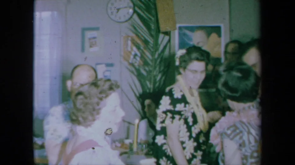 Guests in leis and patterned clothing socialize in a bright corner of a 1961 California private interior.