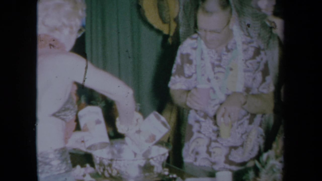 California 1961 party frame with adults around a punch bowl, including a sleeveless woman and a woman in a patterned dress.