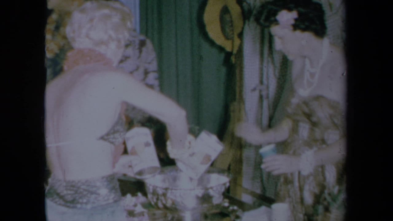 1961 California home-movie frame of two dressed women preparing punch at an indoor party table.