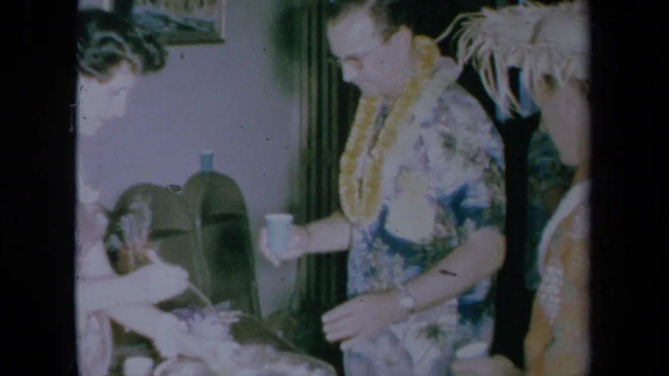 1961 California party frame showing a man with a lei holding a cup beside the punch bowl and other guests.