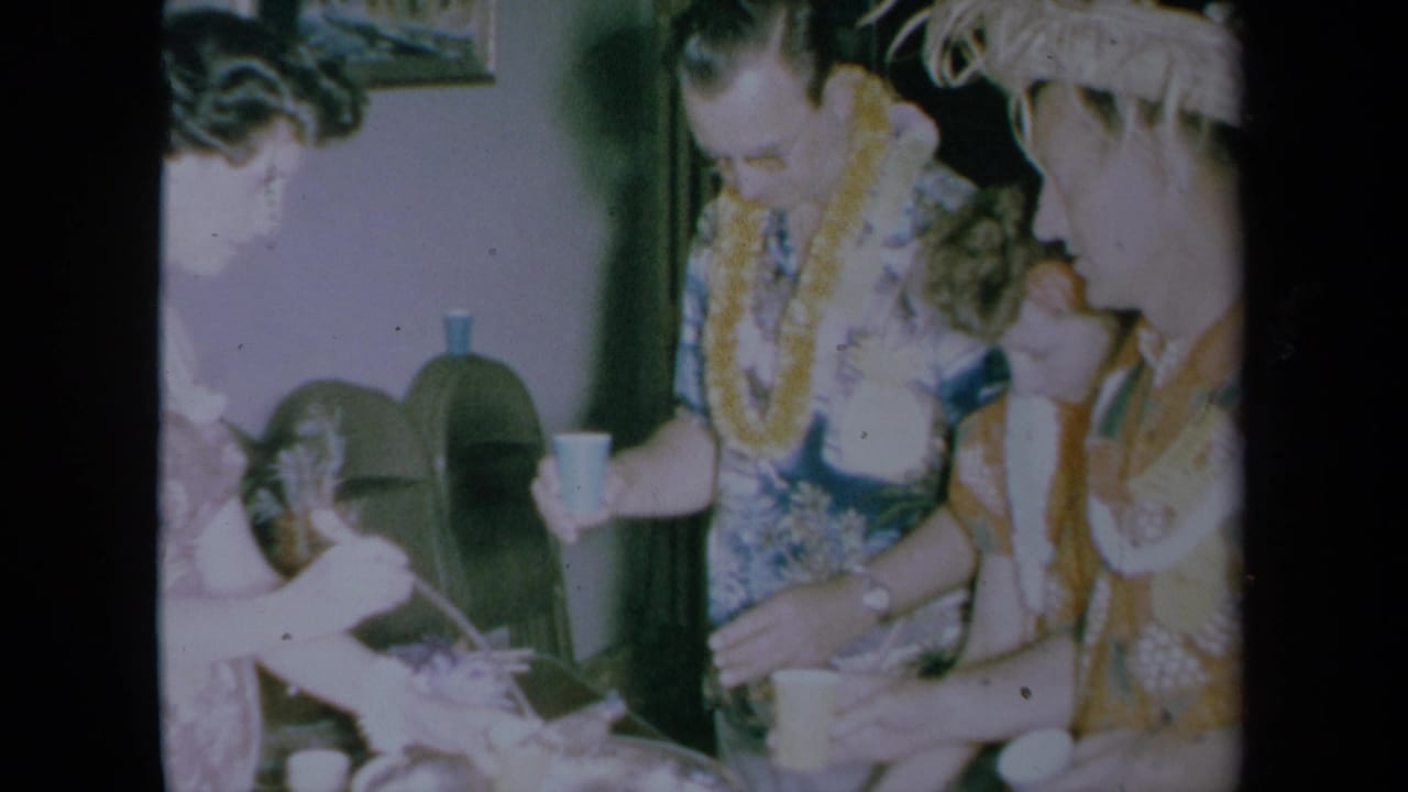 Adults at a 1961 California Hawaiian-themed party lean near a table with cups and a bottle, filmed in soft 8mm color.