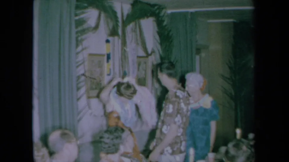 1961 California indoor party footage shows a lei being lifted near a man in an aloha shirt as guests look on.