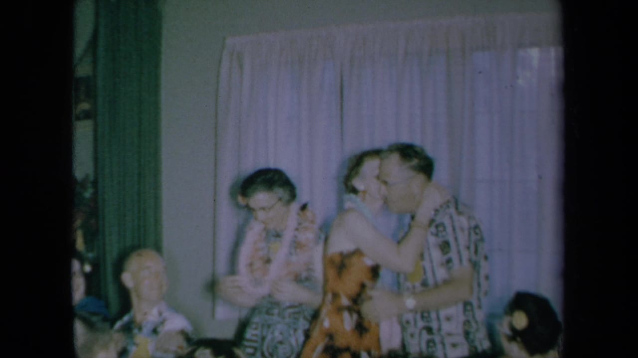 Woman leans in to kiss a man wearing a lei while another guest stands nearby.