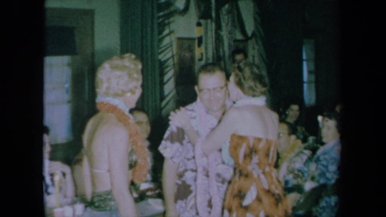 Adults wearing leis and floral party clothes mingle in a California home-movie scene from 1961.