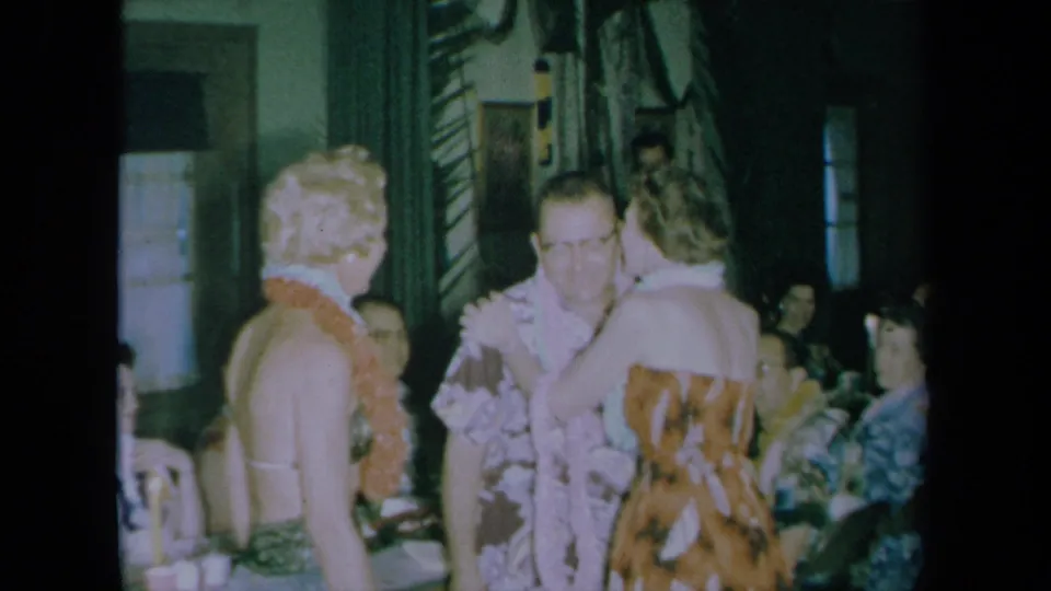 Adults wearing leis and floral party clothes mingle in a California home-movie scene from 1961.