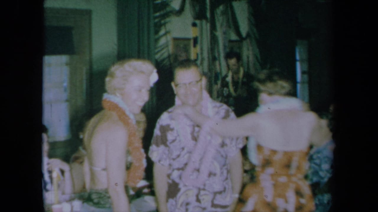 Party guests in leis smile and move together indoors.