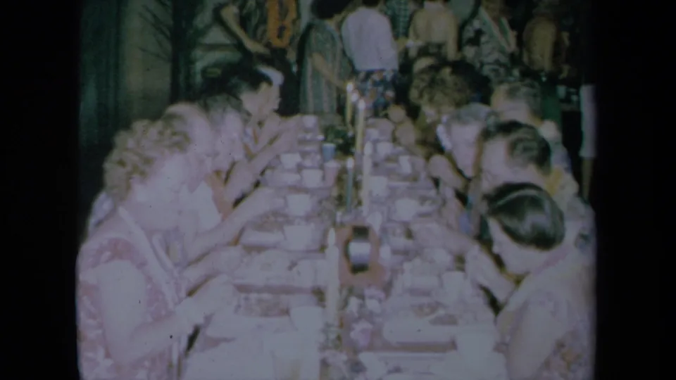 Home-movie frame from California in 1961 showing adults seated close together at a set dinner table.
