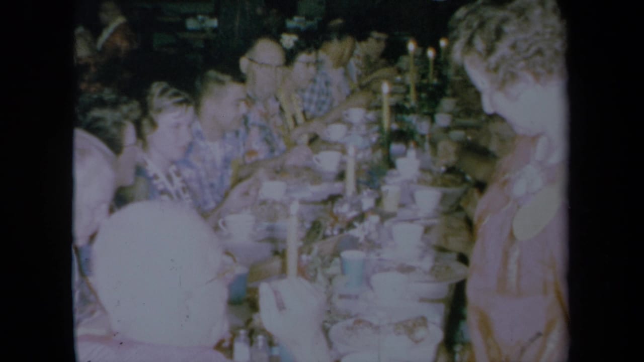 Adults seated around a long candlelit dining table during a holiday meal.