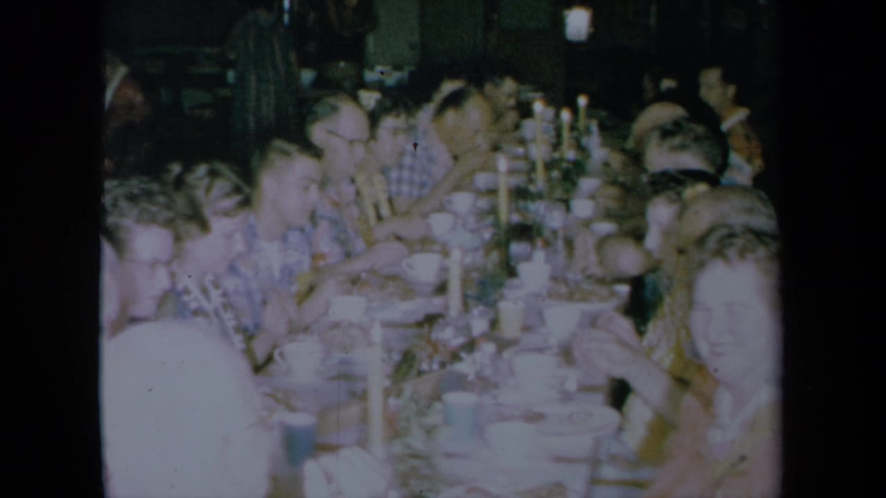 Large group eating at a long table with candles and tableware visible.