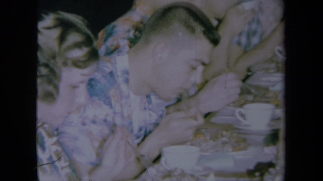 1961 California home-movie frame showing adults at a table with white cups, including a man in a patterned shirt.