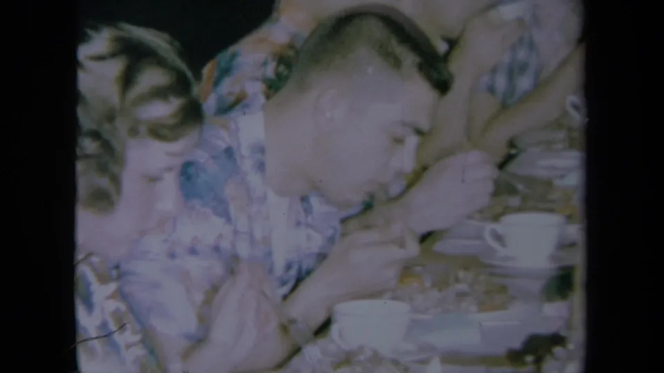 1961 California home-movie frame showing adults at a table with white cups, including a man in a patterned shirt.