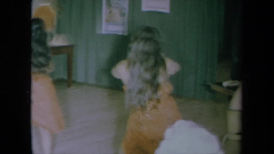 1961 California home-movie frame showing dancers from behind and side as they continue a hula-style routine indoors.