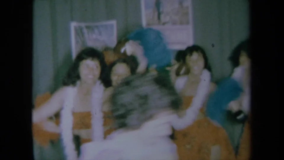 Close 1961 California home-movie view of dancers in leis and grass skirts, with motion blur and a partially obscured foreground figure.