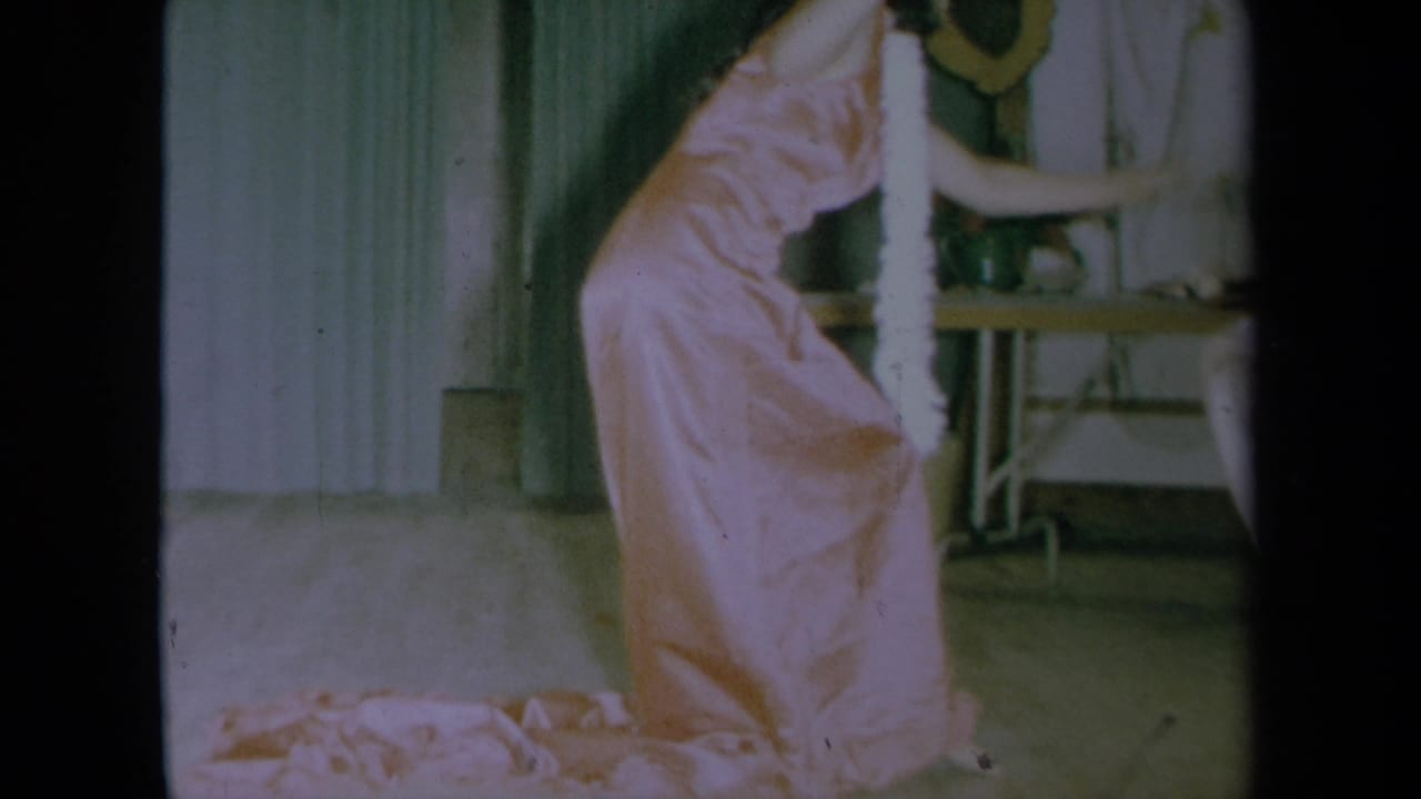 Woman in pink dress leans forward while dancing near a small table.