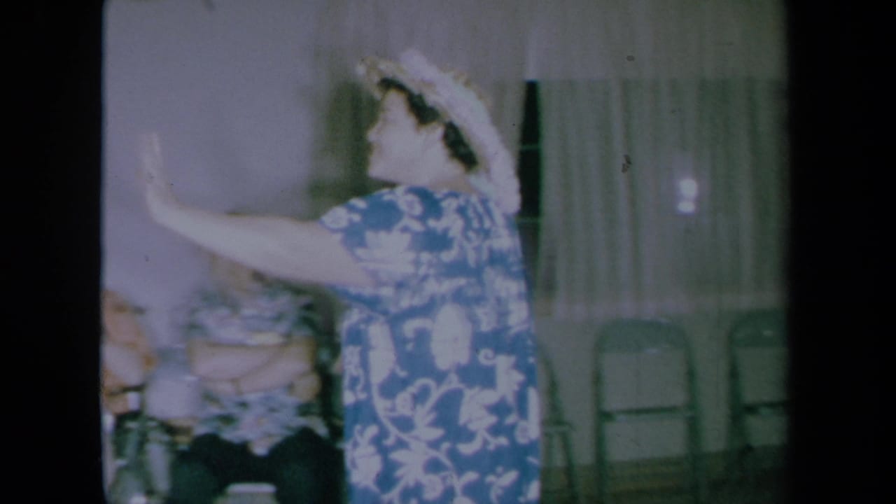 Woman in hat gestures while dancing beside seated adults and folding chairs.