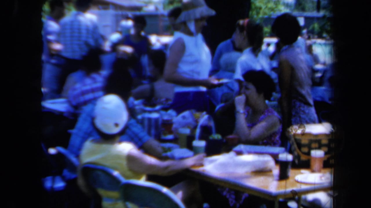 1961 California 8mm frame showing people around picnic tables at a crowded outdoor family gathering.