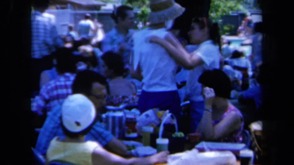 Soft 8mm frame from a 1961 California outdoor gathering, with guests clustered around a picnic table.