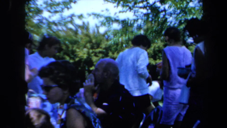 Candid 8mm frame of adults in casual summer clothing gathered outdoors under trees in California, 1961.
