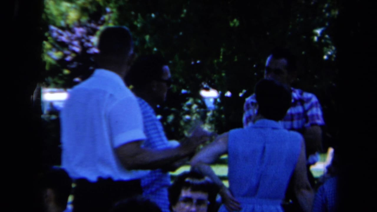 Adults stand together in a shaded park area, partly silhouetted by trees.
