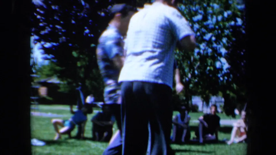 Adults stand and move on a sunny California lawn, with seated spectators visible in the background of the 1961 home movie.