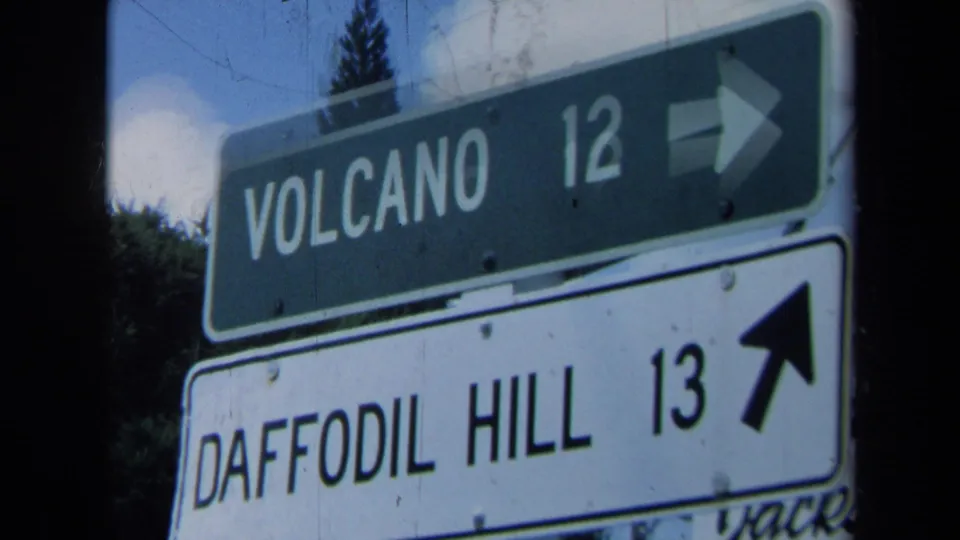 Vintage 8mm close-up of California directional signs for Volcano 12 and Daffodil Hill 13, with right and upward arrows visible.