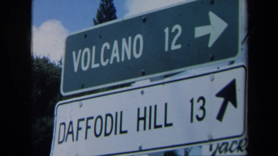 Close 8mm view of California directional signs reading Volcano 12 and Daffodil Hill 13 with arrows.