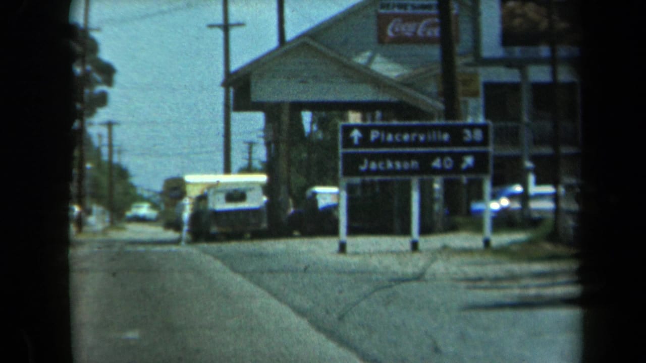 Highway direction sign for Placerville and Jackson beside a roadside building and white van.