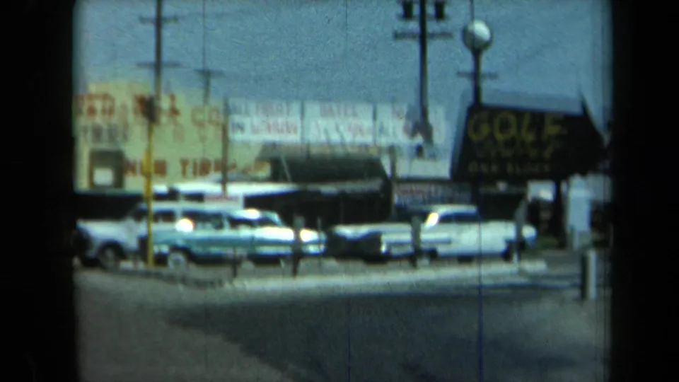 1969 California street view showing parked cars, a dark golf sign, commercial signage, utility poles, and film-frame edge shadows.