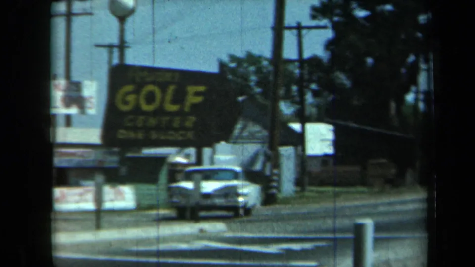 A 1969 California roadside view shows a large golf center sign, classic cars, utility poles, and a road curving past the business frontage.