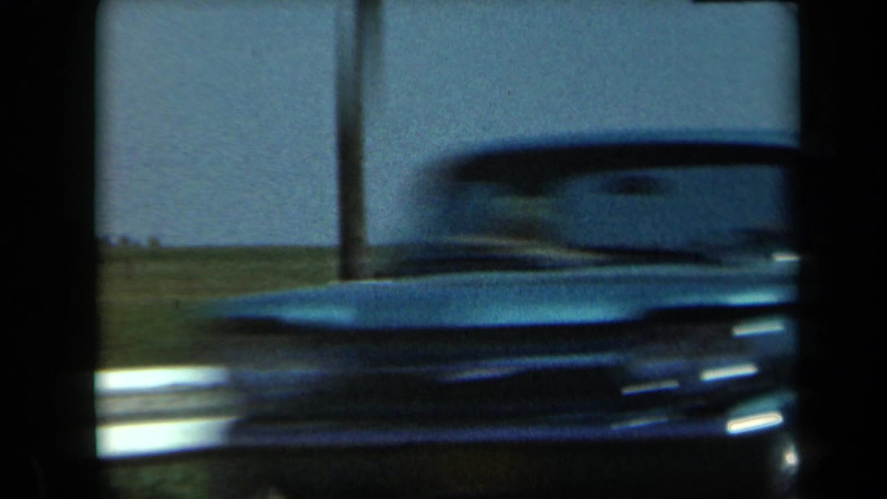 A soft, dark 8mm frame from 1969 California shows a blurred vehicle or roadside foreground before the horse-and-foal view.