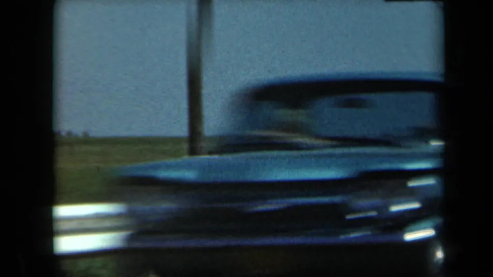 A soft, dark 8mm frame from 1969 California shows a blurred vehicle or roadside foreground before the horse-and-foal view.