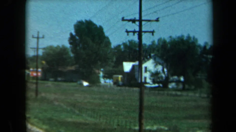 1969 California rural roadside view with a white farmhouse, open field, trees, utility poles, and small structures.