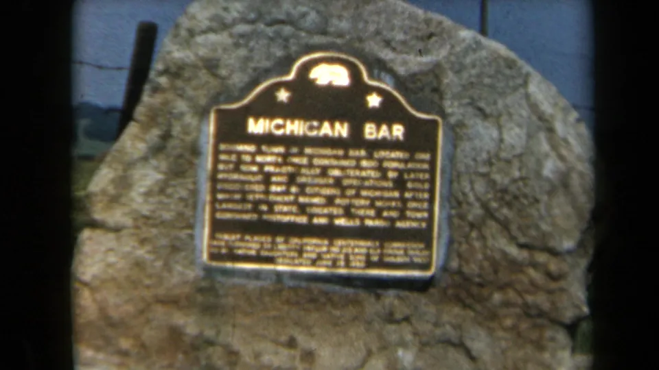 1969 8mm close-up of the Michigan Bar marker in California, framed tightly against the rock surface with readable title text.