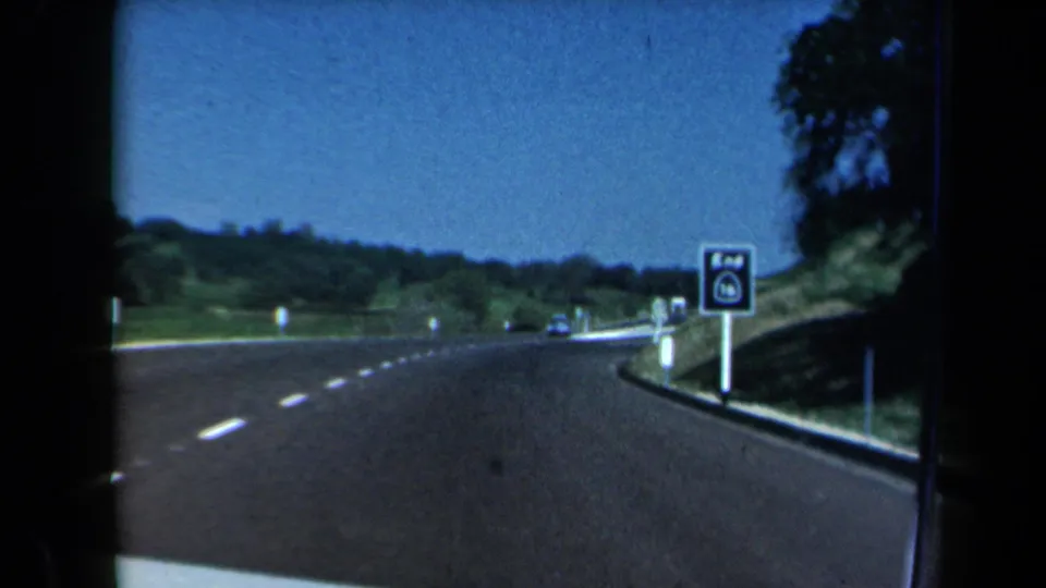 End of the 1969 California highway shot with a route-end sign, distant cars, roadside trees, and rolling hills.