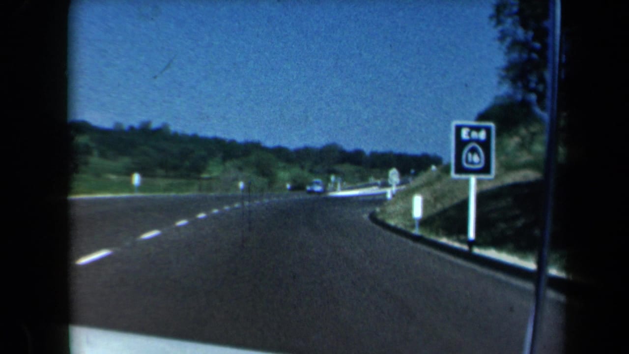 Curving highway seen from inside a vehicle with an end-route sign beside the road.