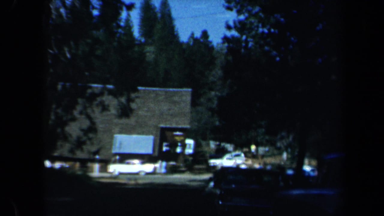 Cars and a small building seen through deep shade and trees.