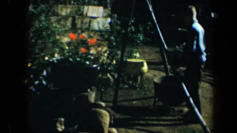 1969 California 8mm frame showing a shaded garden path area with planters, flowers, and a distant standing person.