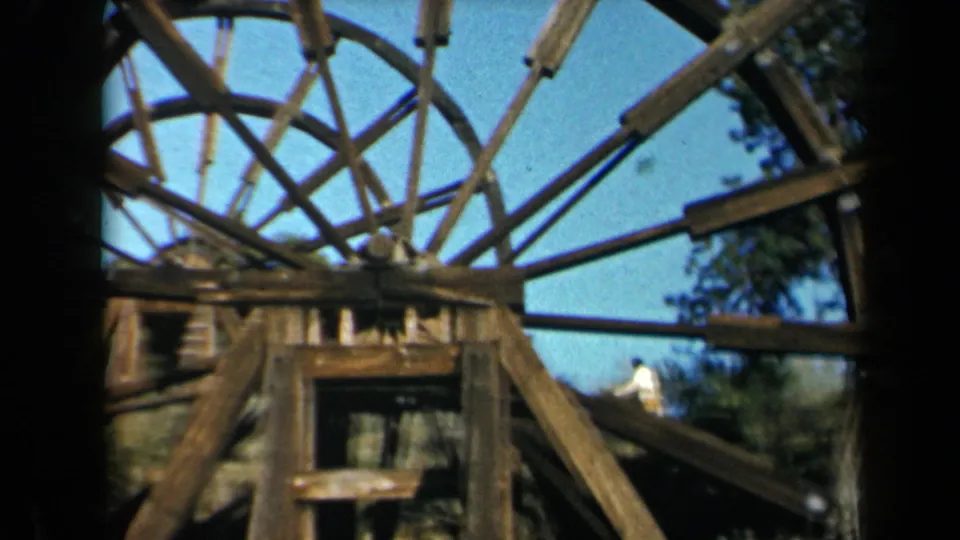 1969 California 8mm frame showing the wooden waterwheel and a distant adult figure moving near the structure.