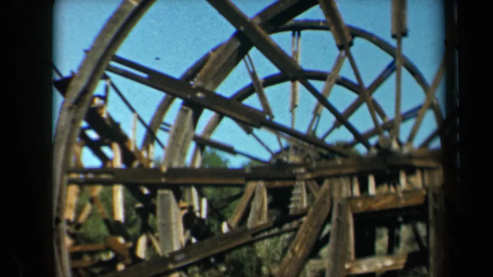 Final 1969 California 8mm frame of a rustic wooden waterwheel and beams against a clear blue sky.