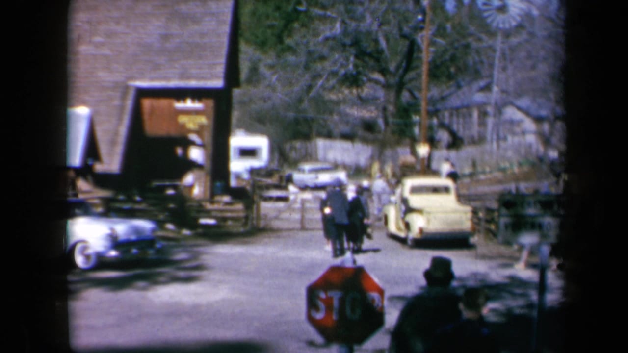Pedestrians and parked cars near a stop sign on a small-town street.