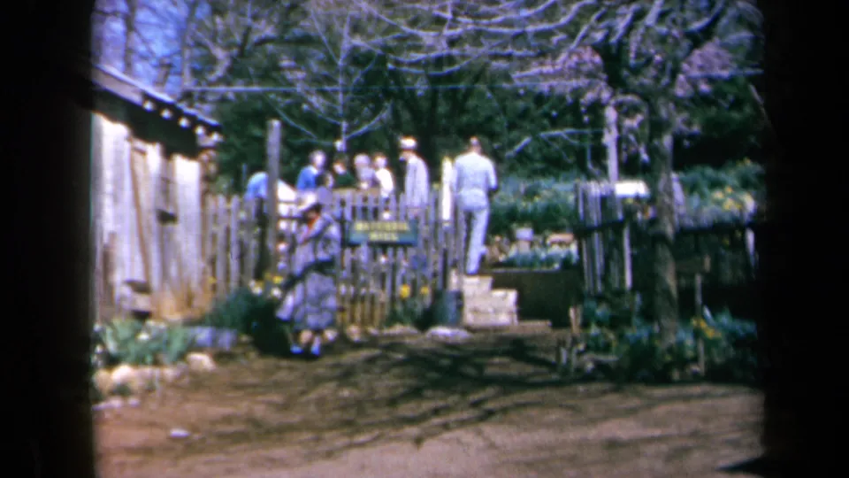 A handheld 8mm view shows visitors milling near a wooden fence, dirt path, and rustic garden building at Daffodil Hill.