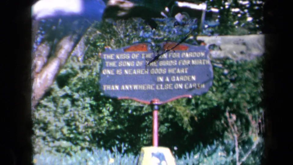1969 California 8mm frame showing a dark garden verse sign on a red post, seen through soft focus and visible film borders.