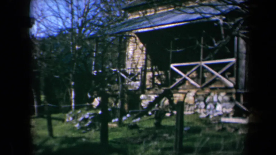 As the camera pans, the boy moves out of prominence and the rustic barn porch, railing, fence, and yard debris become central.