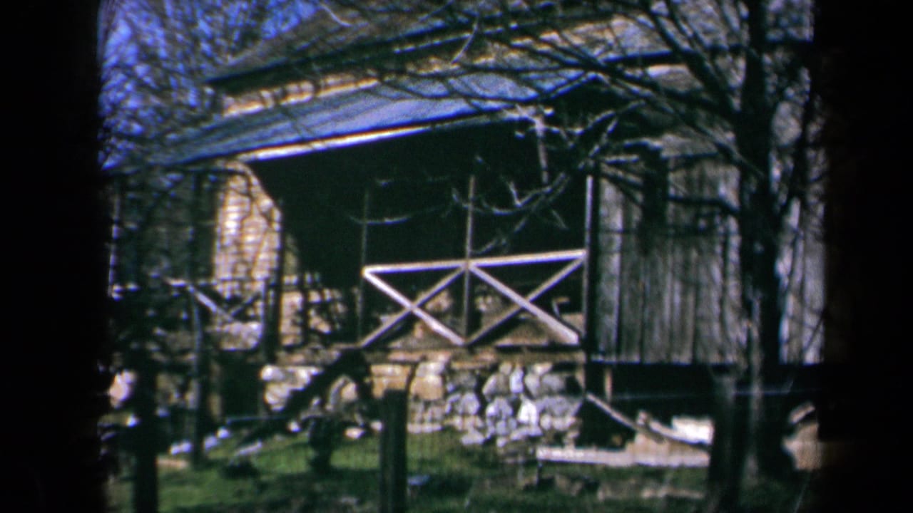 Rustic wooden cabin with stone foundation and X-braced porch railing behind trees.