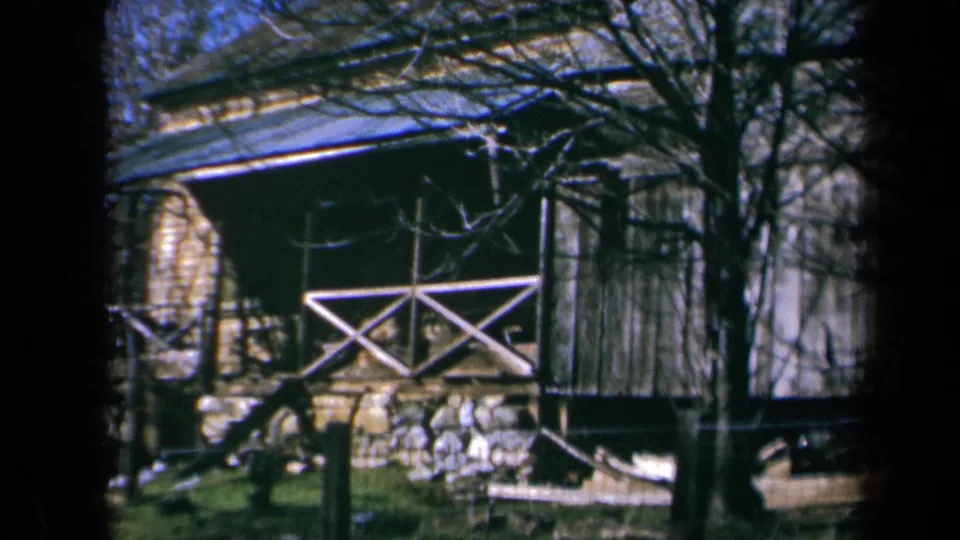 1969 California home-movie view of the cabin facade, porch rail, stonework, and surrounding leafless trees.