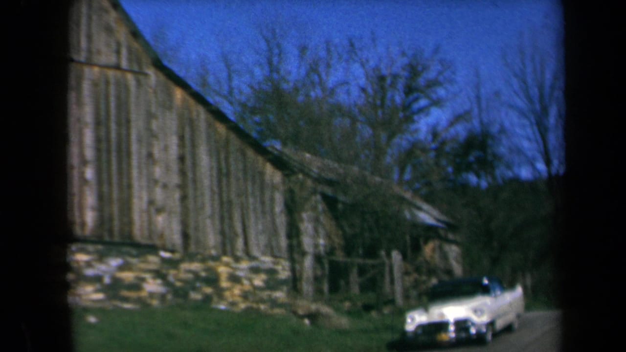 1969 California 8mm frame showing a white convertible near a weathered barn with stone foundation and bare trees.