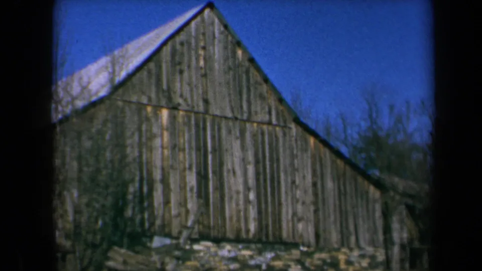 1969 California 8mm frame showing the side of a weathered barn, sloped roof, brush, and blue sky.